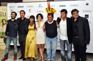 Seven people with their arms around each other in front of a large board carrying the word Xingu and sponsors’ logos