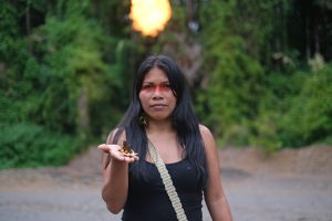 Nemonte Nenquimo, co-founder of Ecuador-based nonprofits Ceibo Alliance and Amazon Frontlines, holds a dead butterfly in her hand near a gas flare at one of Ecuador’s largest oil fields in the northern Ecuadorian Amazon. Credit: Sophie Pinchetti/Amazon Frontlines