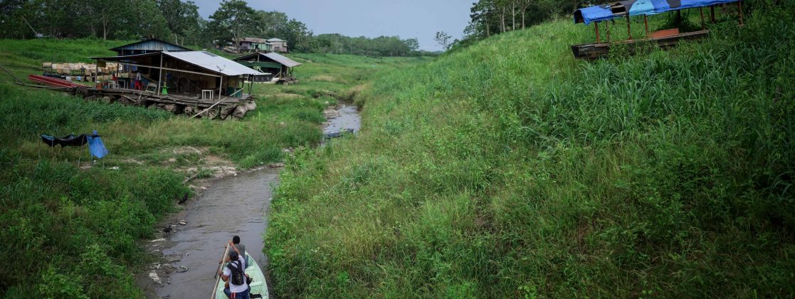 People maneuver by boat through the low water levels of a tributary that connects with the Amazon River, in Isla de la Fantasia, on the outskirts of Leticia, Colombia, Oct. 20, 2024. (AP Photo/Ivan Valencia, File)